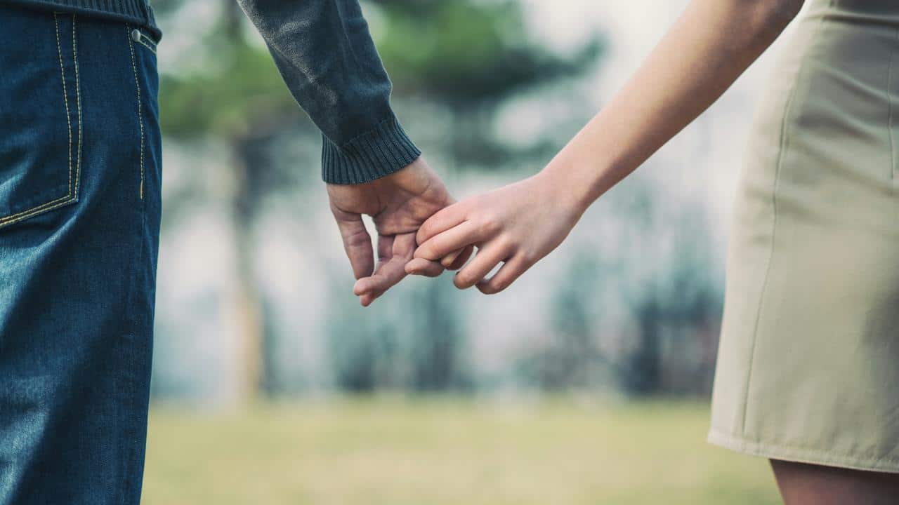 A couple holding hands with fingers gently intertwined.