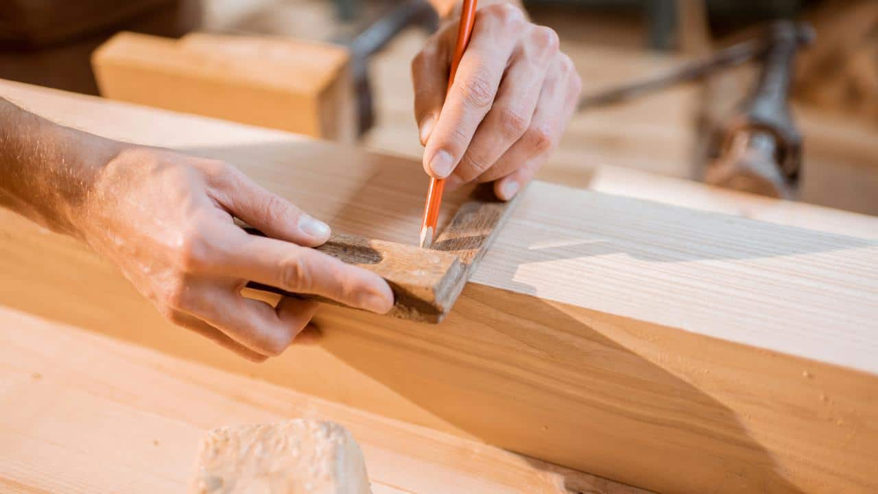 A person marking a wooden plank with a pencil and square.