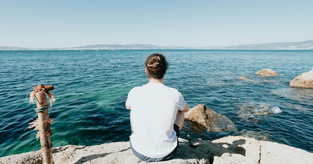 A person sitting on a rocky shore, looking out over the ocean.