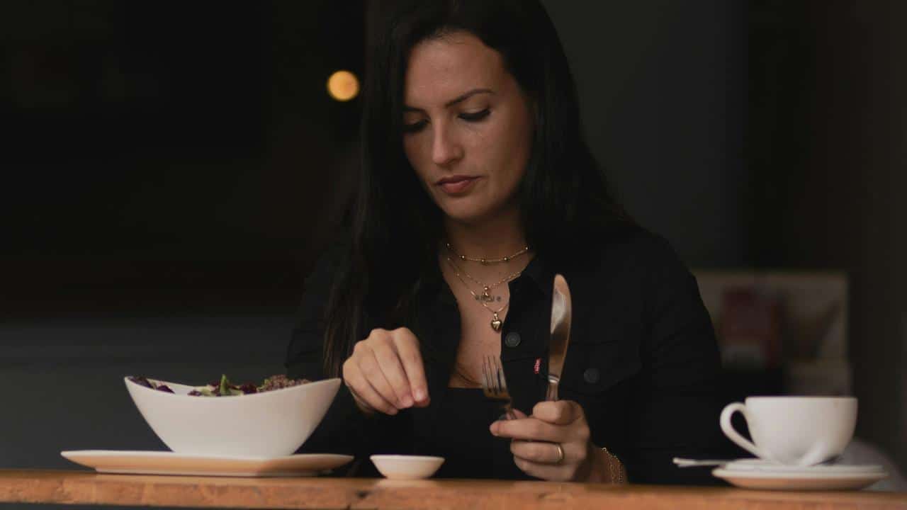 A woman sitting at a table eating a salad with a cup of coffee nearby.