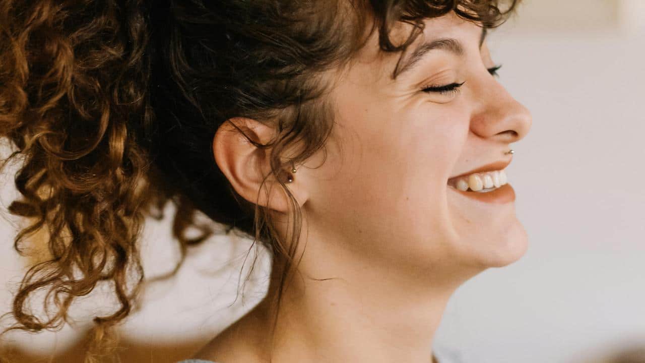 A smiling woman with curly hair laughing in profile.