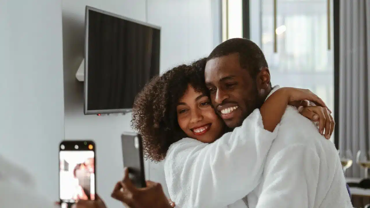 A couple hugging and smiling while taking a selfie indoors.