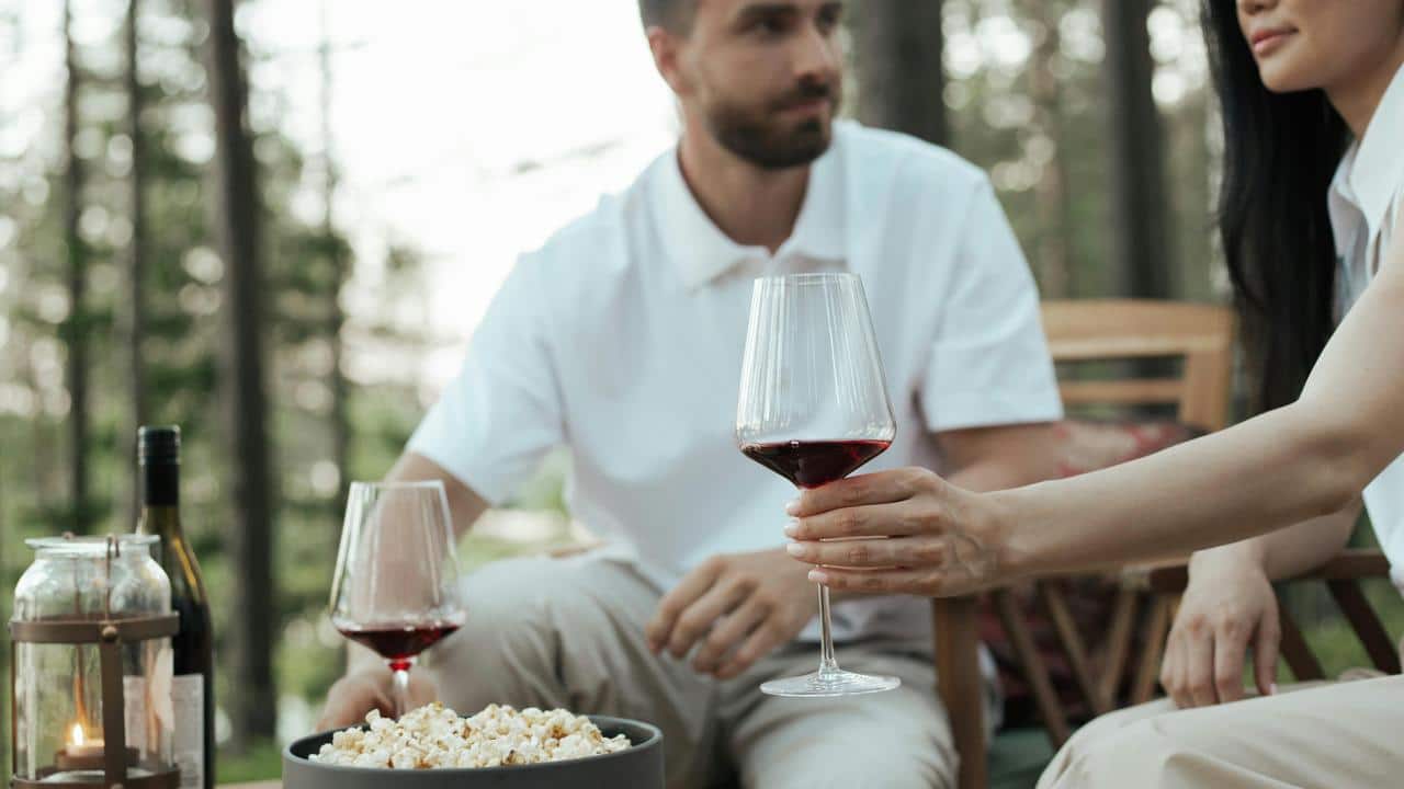 A couple sitting outdoors enjoying wine and popcorn together.