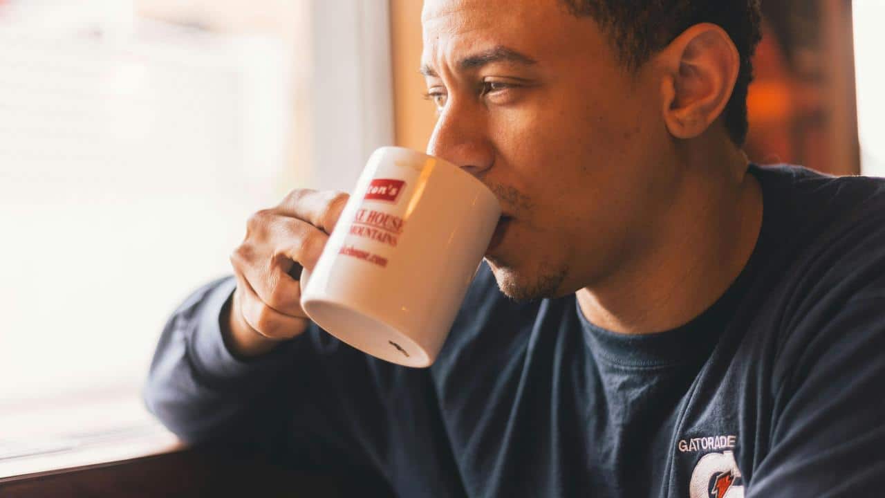 A man drinking from a coffee mug while looking out a window.