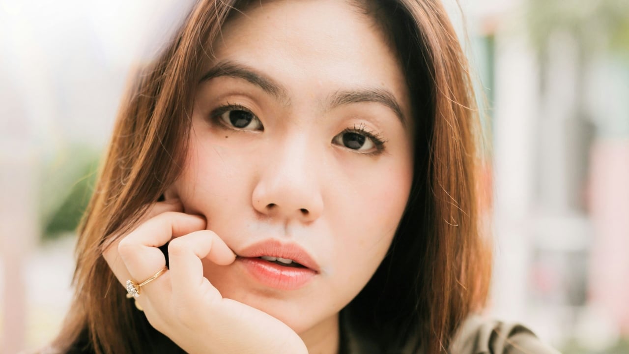 Extreme close-up of a woman’s face resting her chin on her hand with a ring.