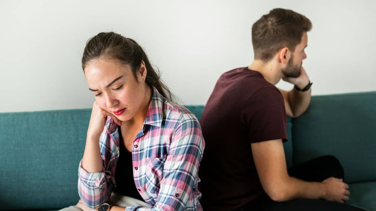 A man and woman sit back-to-back on a teal sofa while looking in opposite directions.