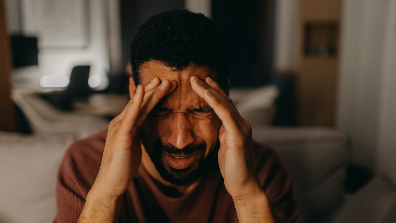A distraught man holding his temples with both hands, looking stressed and in pain.