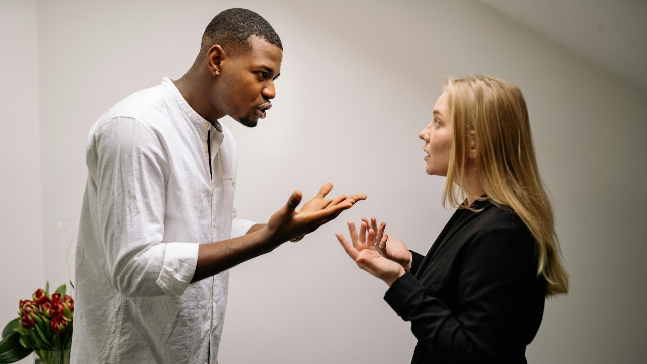 A man and a woman stand facing each other while gesturing with their hands during a conversation.