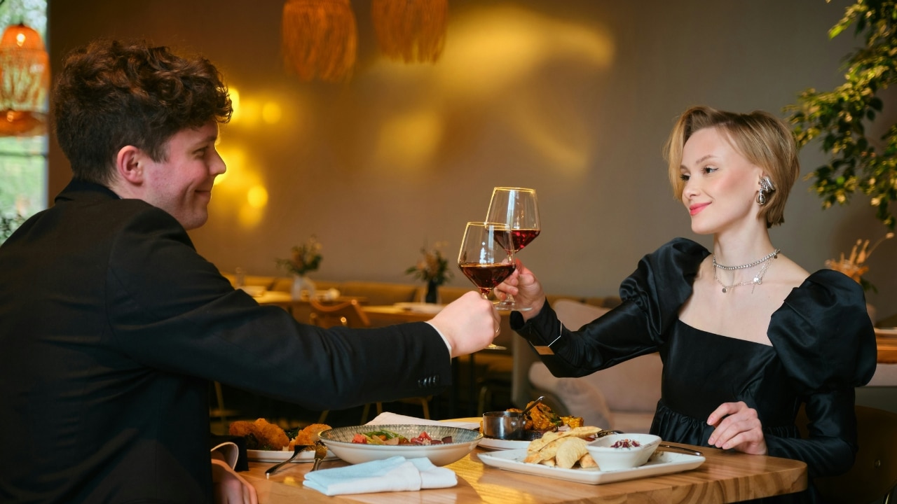 A man and a woman in formal attire toast with wine glasses at a dinner table.