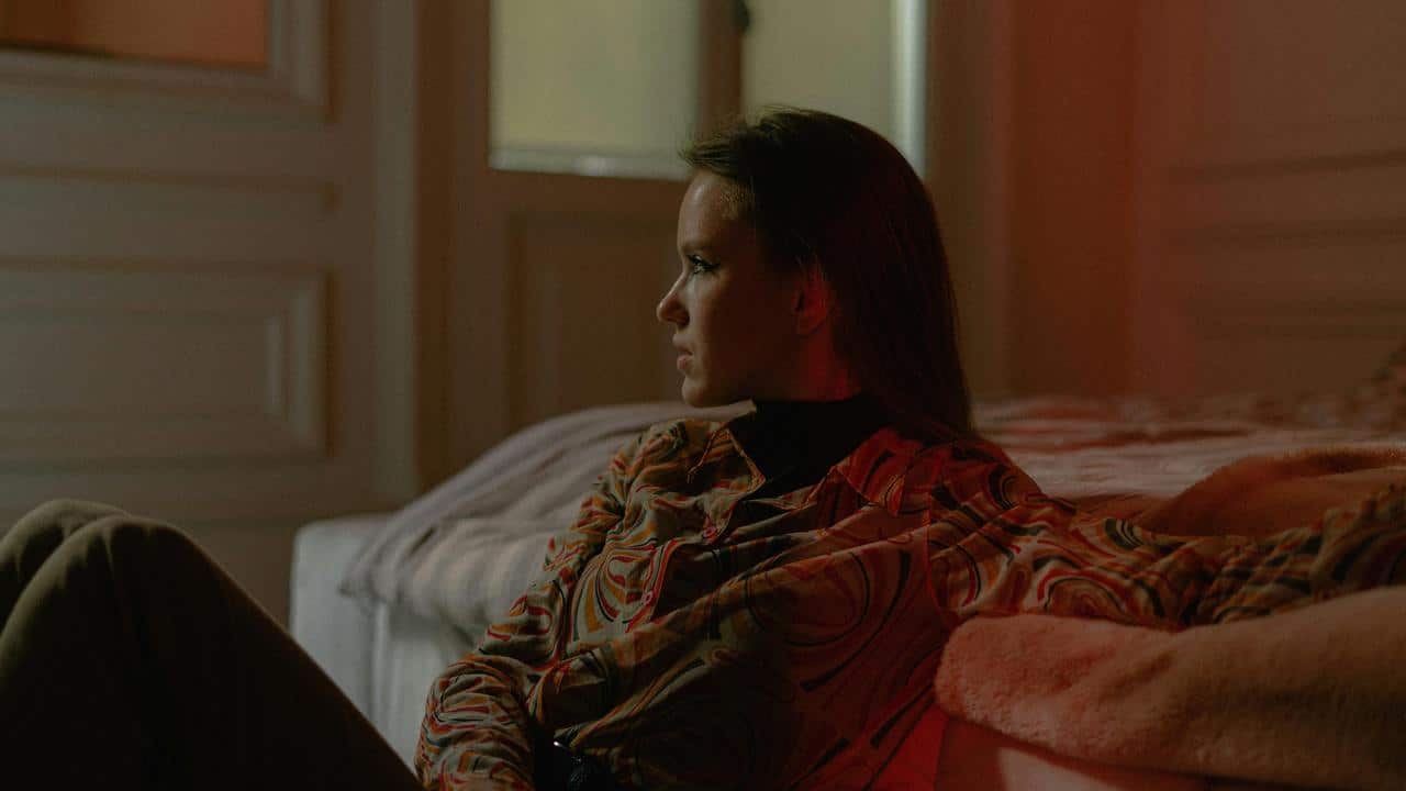 A woman sitting on a bed and looking thoughtfully into the distance.