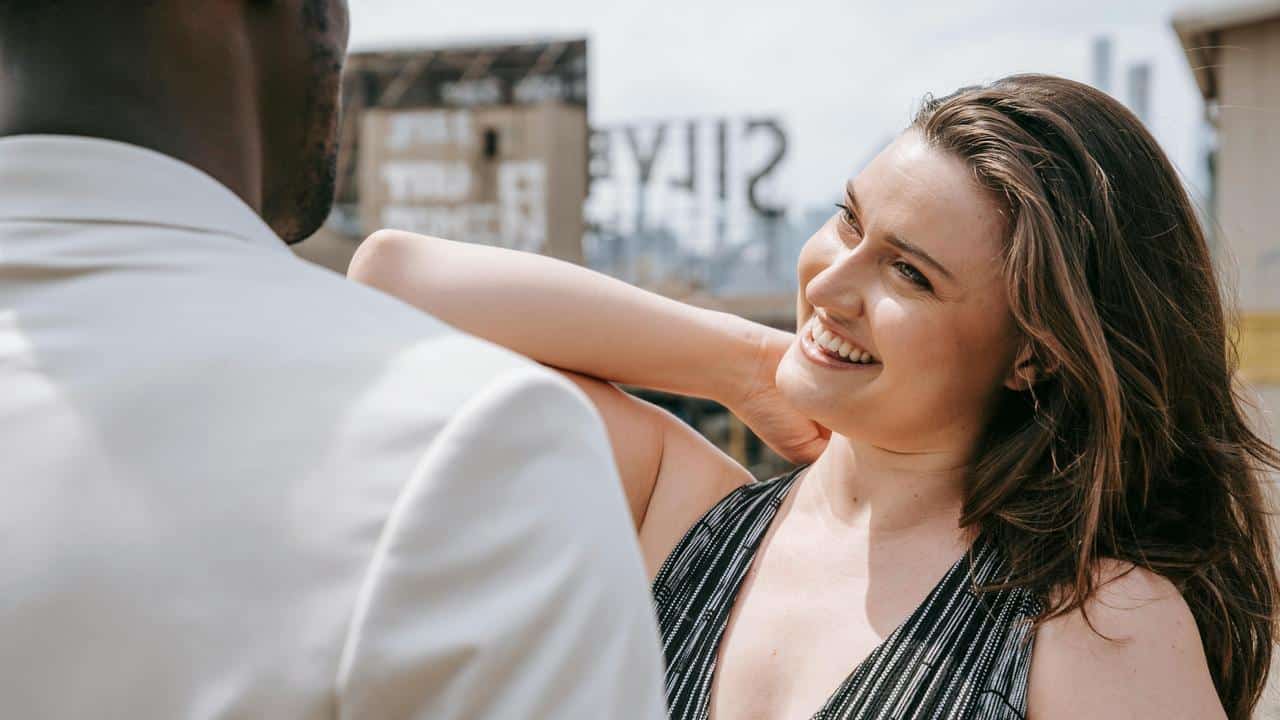 A smiling woman talking to a man outdoors, leaning in with a relaxed expression.