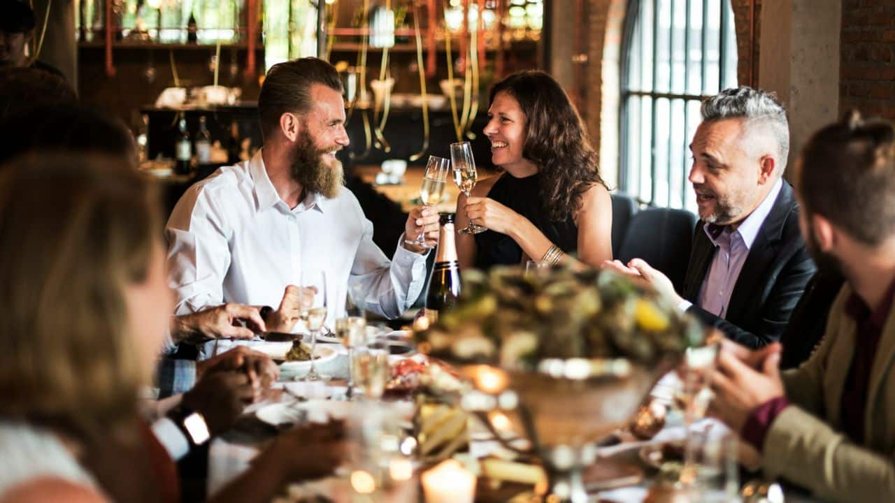 People sit around a dinner table while a man and woman toast with champagne glasses.