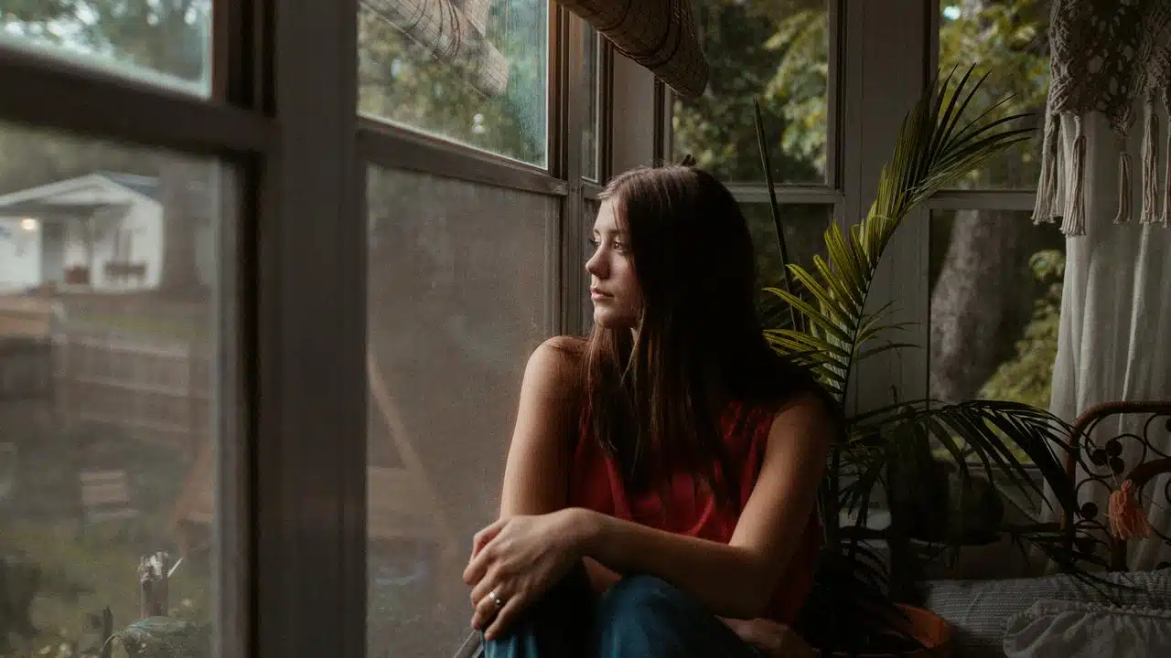 A woman sitting by a window, looking outside thoughtfully.