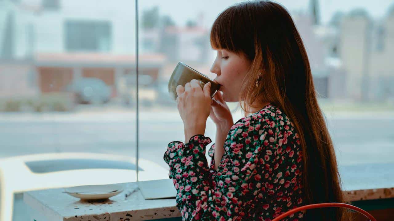 A woman sipping a drink while sitting by a window.