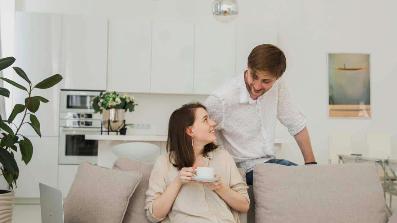 A couple smiling at each other in a bright living room.