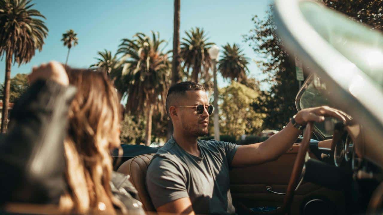 A man driving a convertible with a woman in the passenger seat on a sunny day.