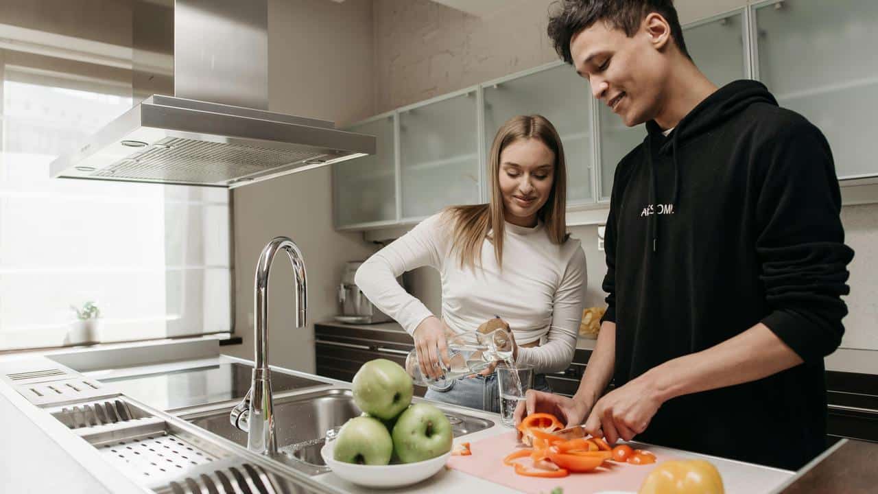 A couple cooking together in a modern kitchen, smiling and chatting.