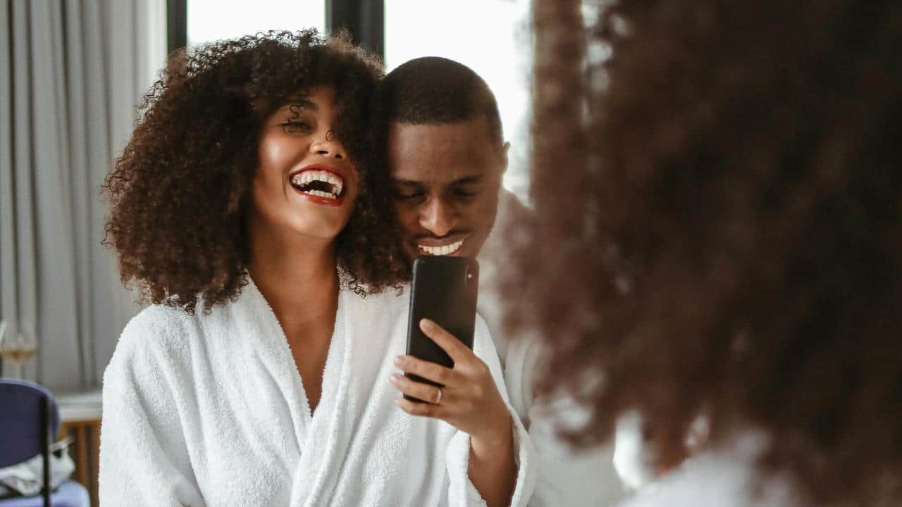 A couple in bathrobes laughing and taking a selfie together.