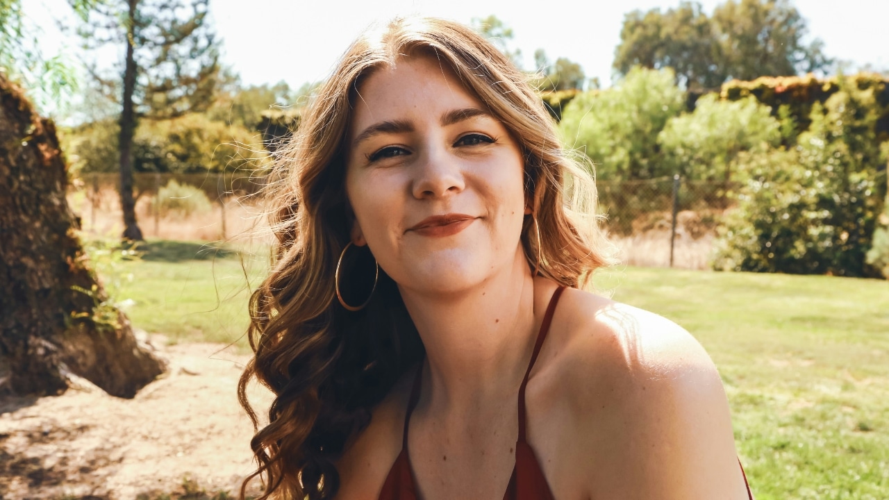 Close-up of a woman with wavy hair and large gold hoop earrings in a park.