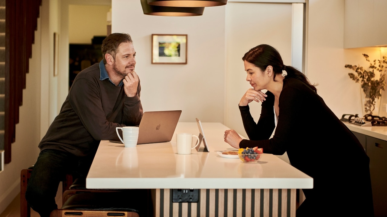 A man and woman sit across from each other at a kitchen island with a laptop.