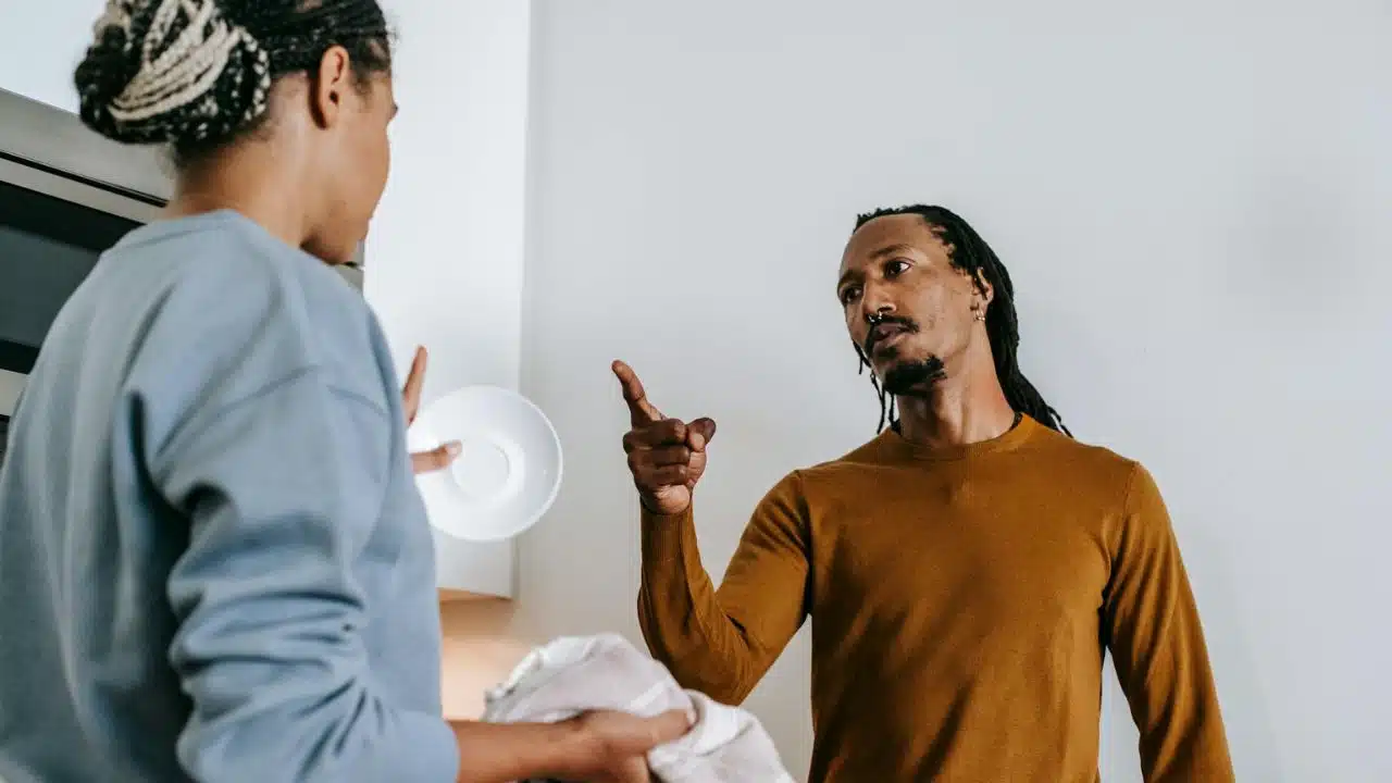 A man with dreadlocks points his finger while speaking to a woman holding a saucer.