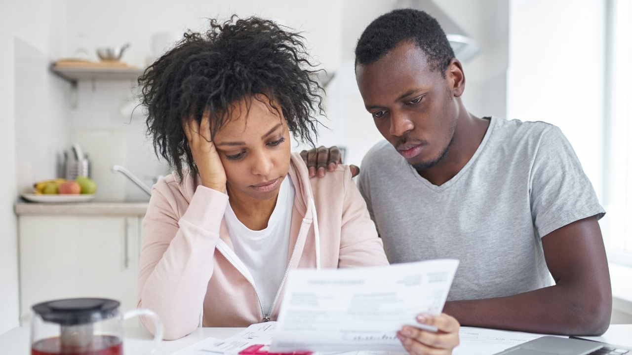 A woman leans her head on her hand while looking at papers with a man.