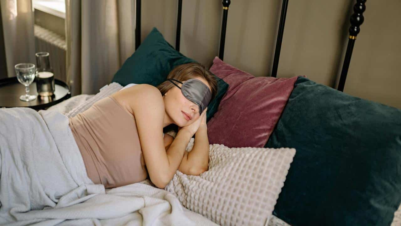 A woman sleeping on a bed wearing an eye mask, resting on pillows.