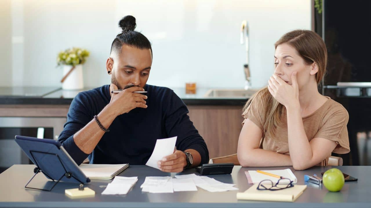 A man and woman sit at a table looking at several papers and a calculator.
