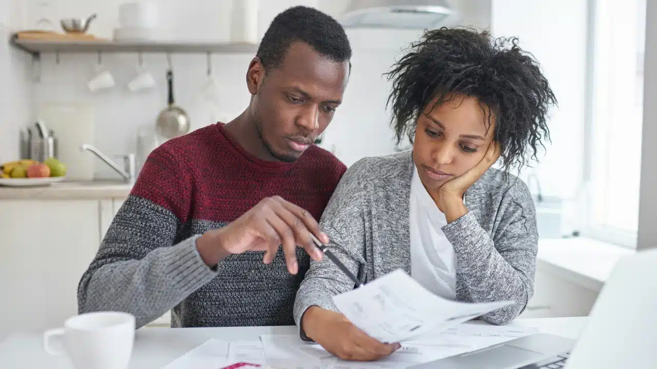 A man and woman sit at a table reviewing several papers and a laptop together.