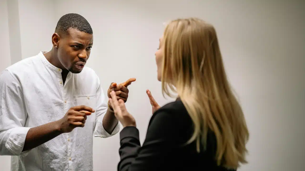 A man in a white shirt points his finger while talking to a blonde woman.