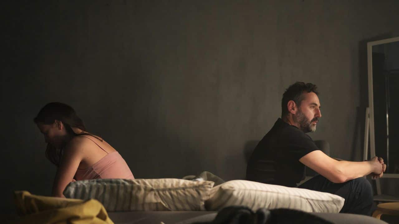 A man and woman sitting on a bed with their backs turned toward each other.