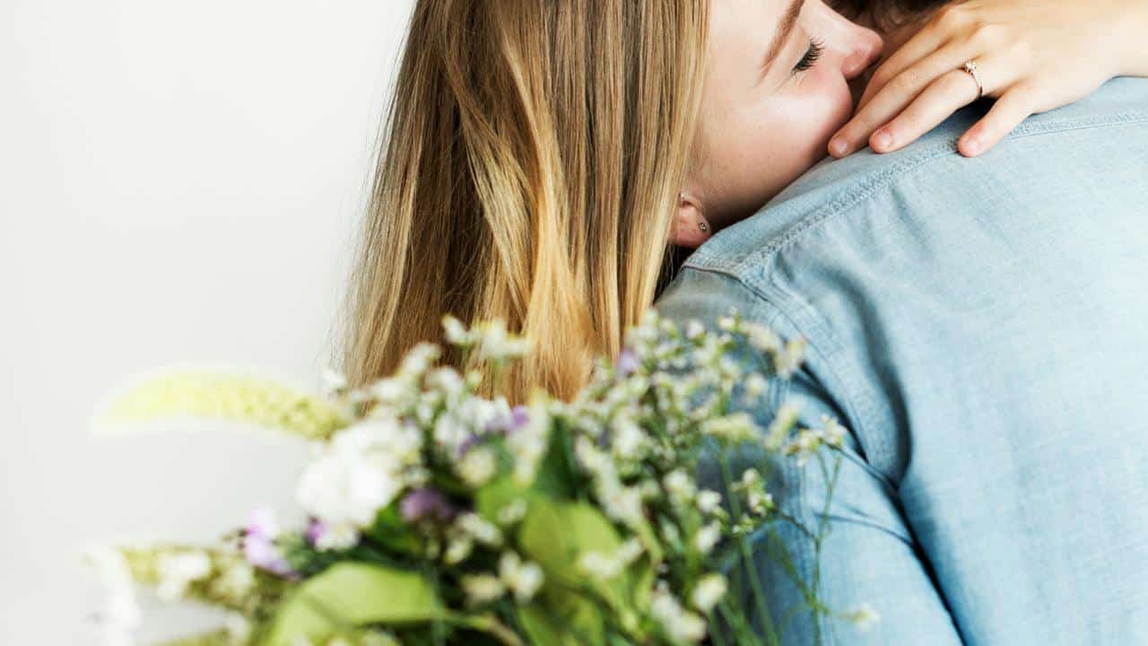 A woman hugs someone while holding a bouquet of flowers.