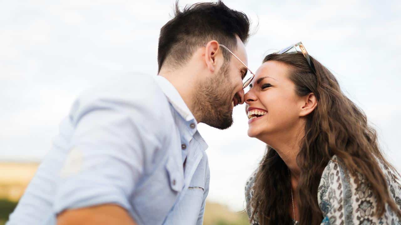A laughing couple leans in close, smiling with their noses touching.