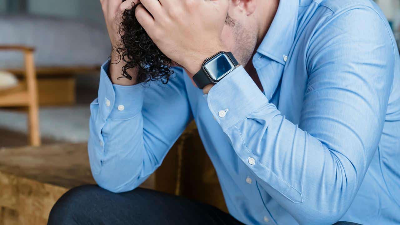 A man holding his head in stress while sitting down.