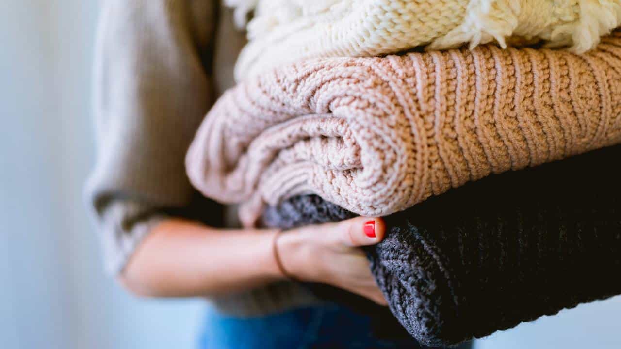 A person holding a stack of folded knitted sweaters.