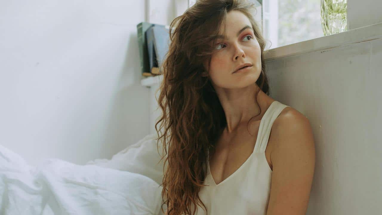 A woman sitting by a window, gazing away.