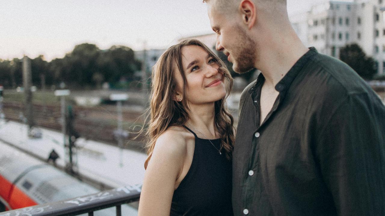 A couple smiling at each other while standing near a train station.