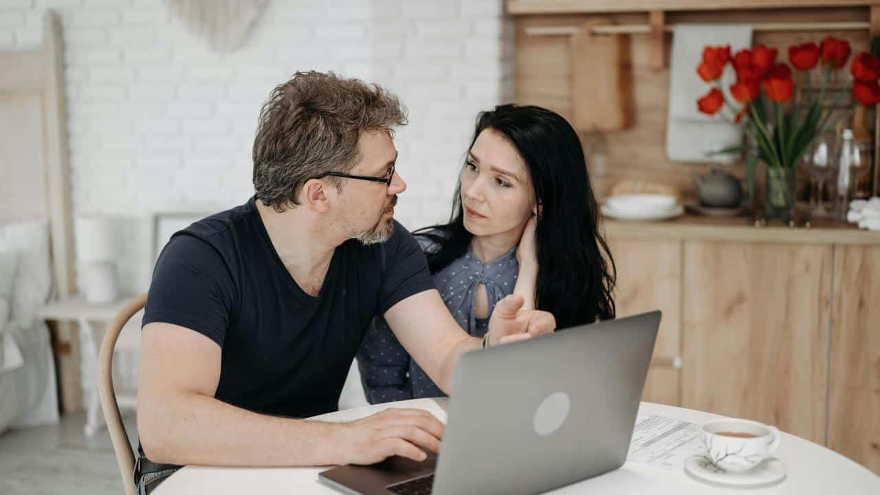 A couple talking while looking at a laptop at a table.