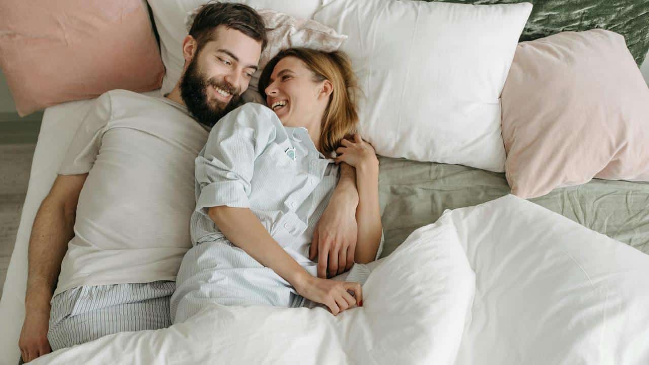 A couple lying in bed together, smiling and enjoying a cozy moment.