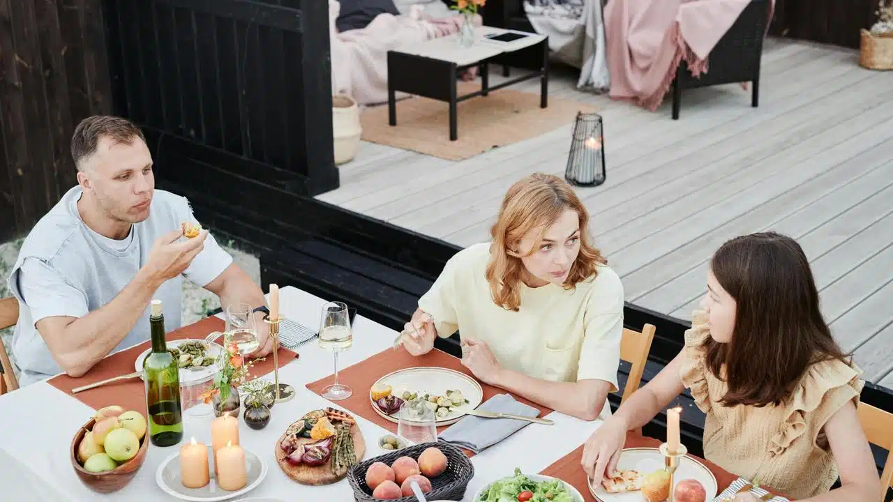 A family eating together at an outdoor table with food and drinks.