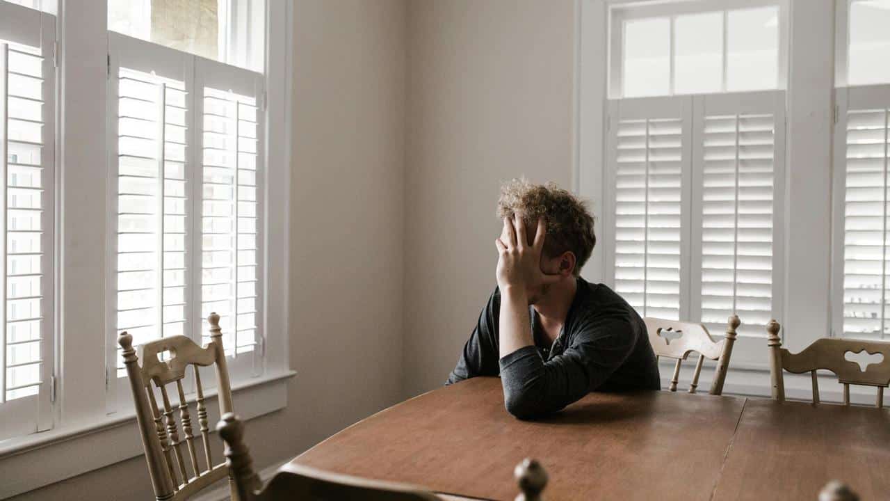 A man sitting at a table with his head in his hand near a window.