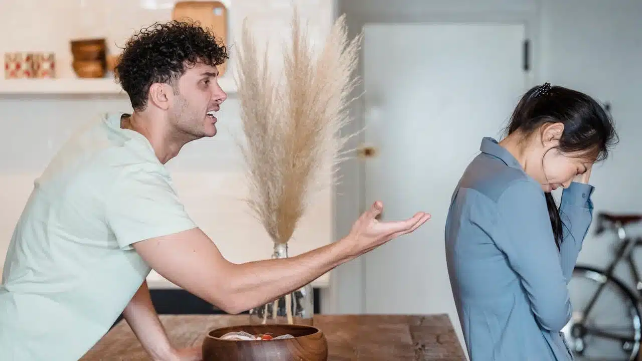 A man is aggressively yelling and gesturing at a woman who is turned away from him