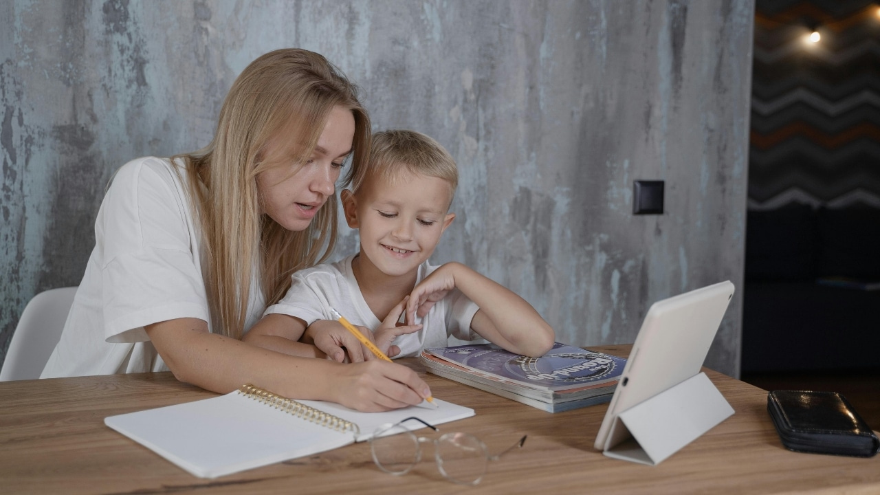 A woman and a young boy sit at a table while working on a notebook together.