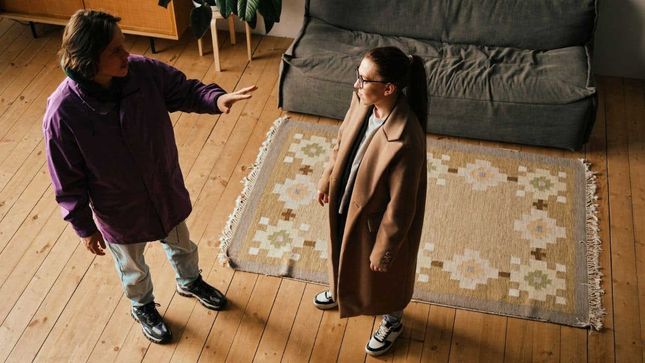 A person in a purple jacket gestures toward a woman in a long brown coat.