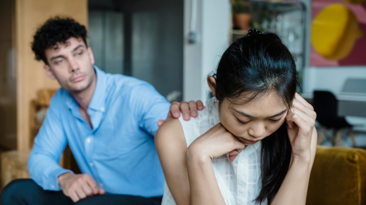 A man places his hand on the shoulder of a woman who is looking downward.