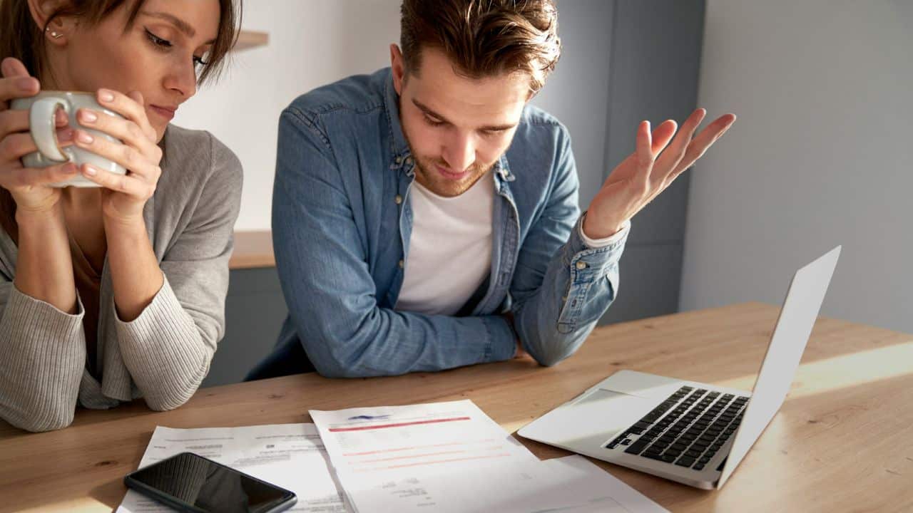 A man looks at papers and a laptop while a woman holds a mug.