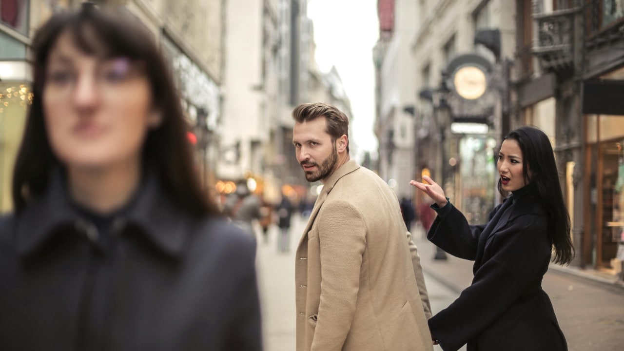 A man turns to look at a woman walking by while another woman gestures behind him.
