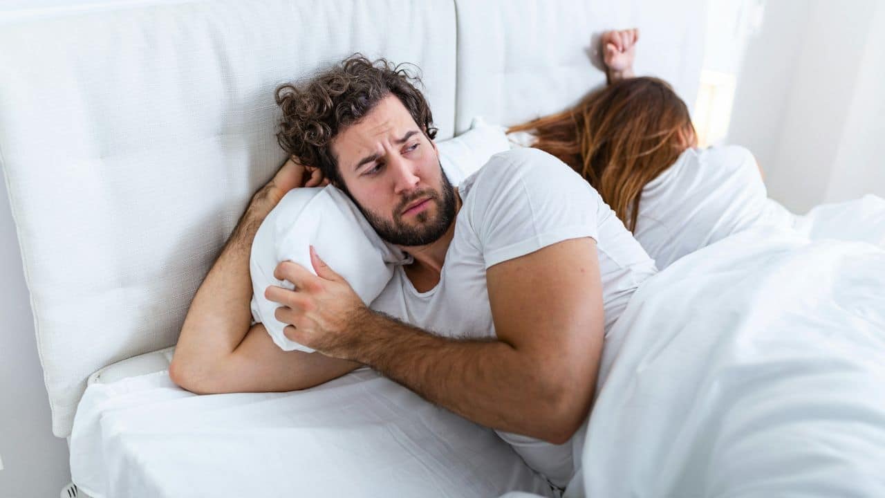 A man lies in bed looking away while a woman lies with her back turned.