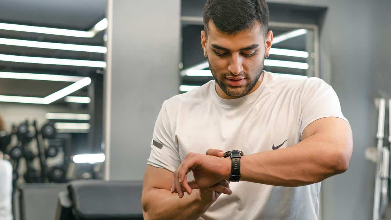 A man in a gym checking his smartwatch during a workout.