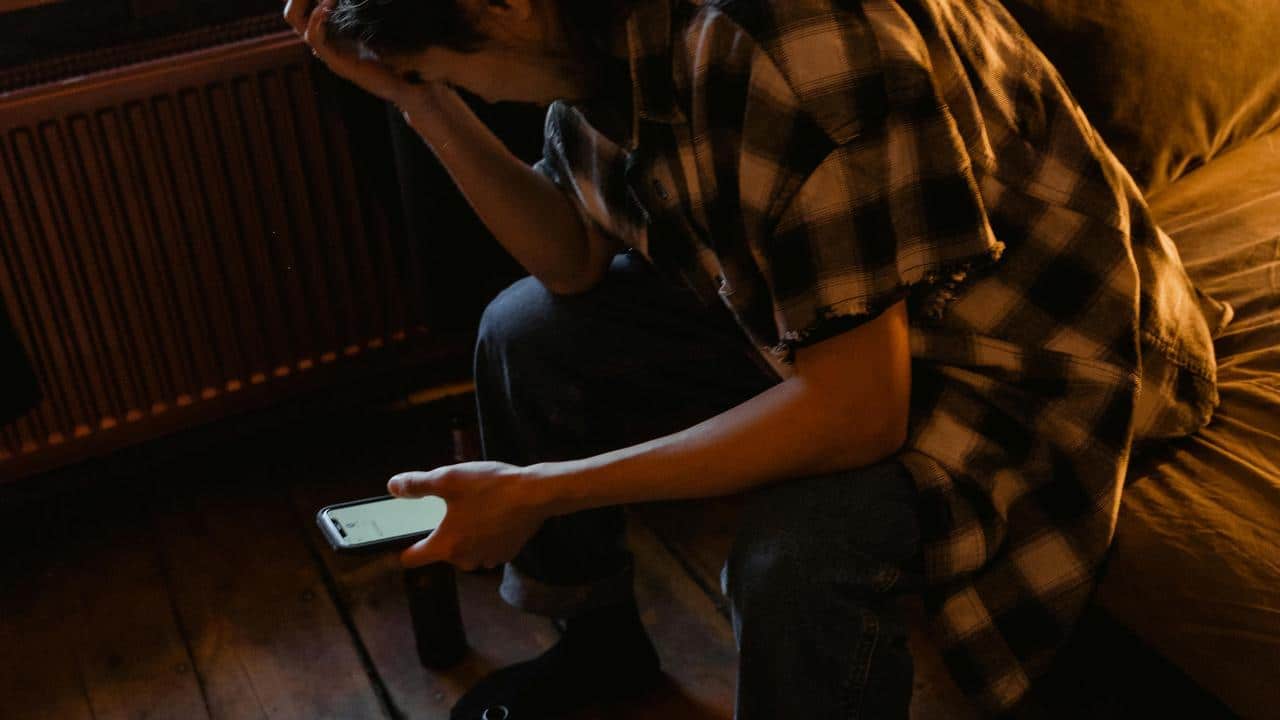 A person sitting and looking at a phone with their head in their hand.